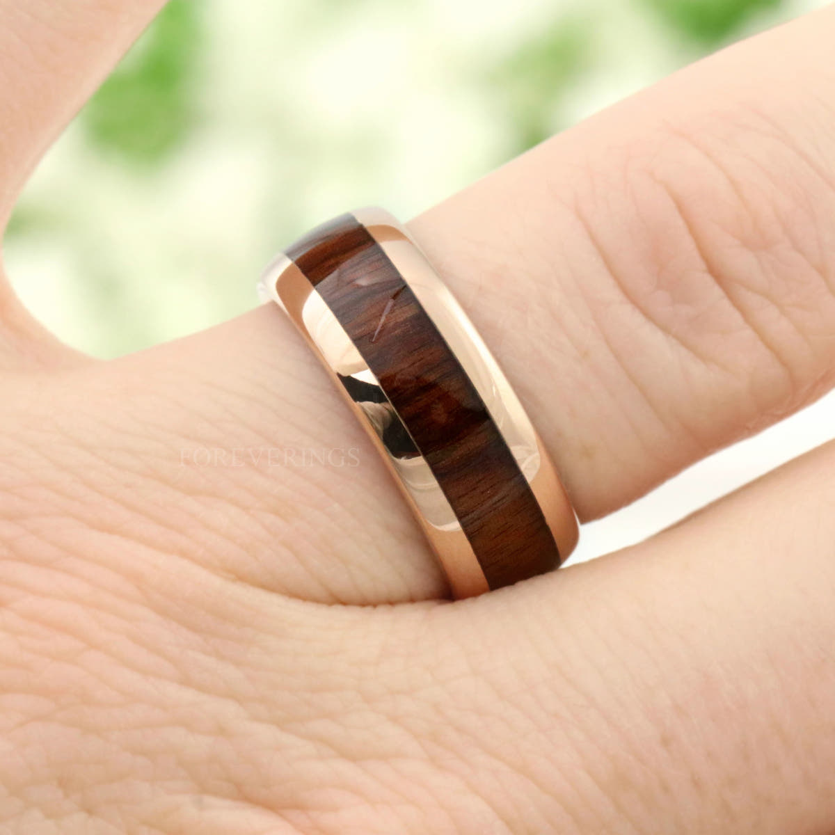 Men's rose gold tungsten wedding band with koa wood inlay worn on a finger