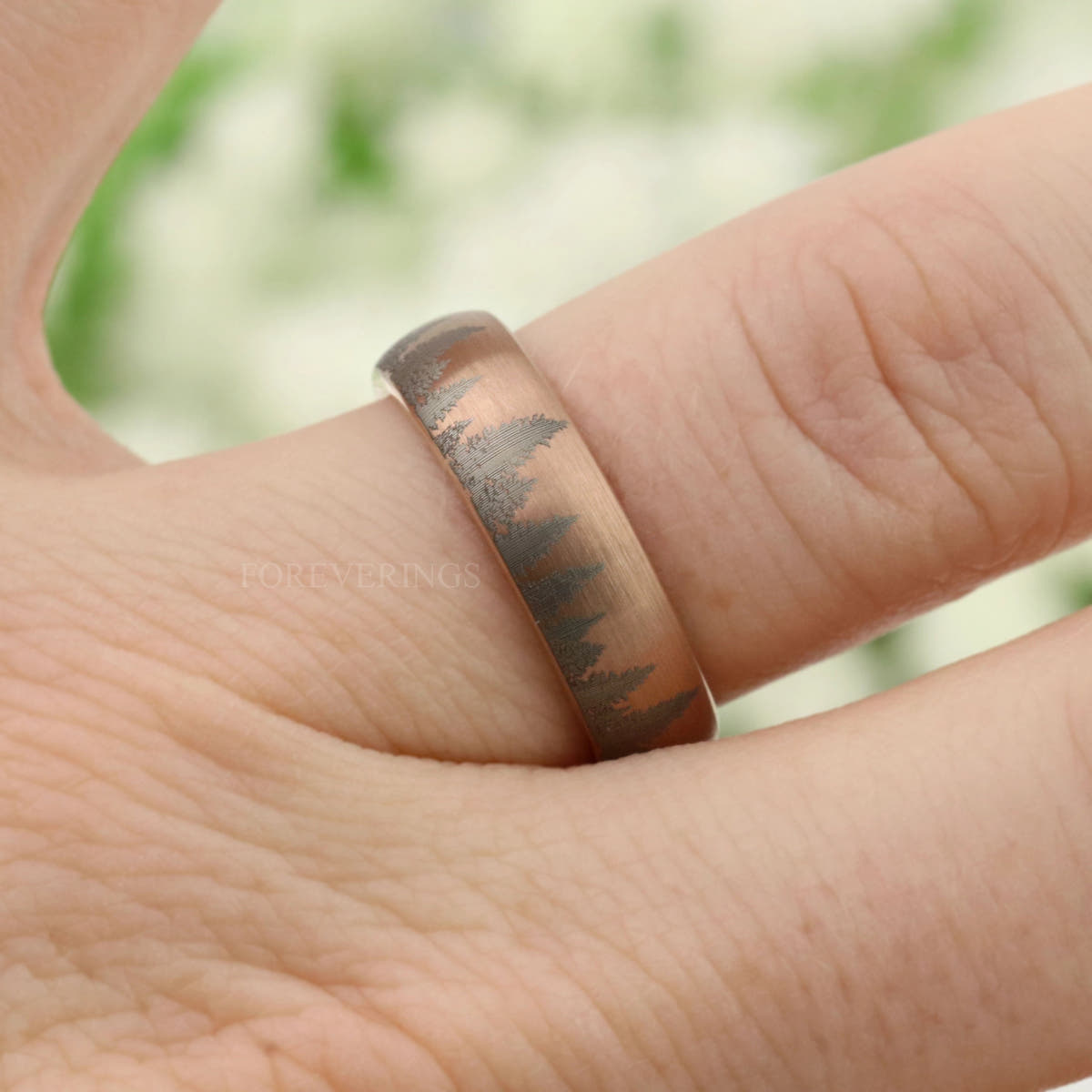 Men's matte rose gold tungsten forest band on a finger, angled view