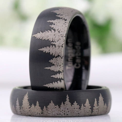 Men's matte black tungsten wedding bands with etched pine tree line, one standing on another