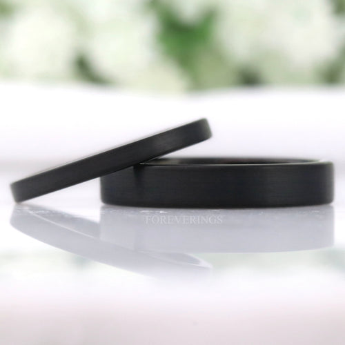 Thin matte black tungsten wedding bands in 2mm and 4mm, flat profile, leaning together