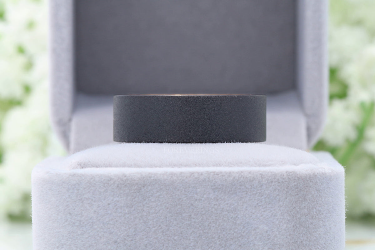 Black tungsten whiskey barrel wedding band sitting in a gray velvet ring box