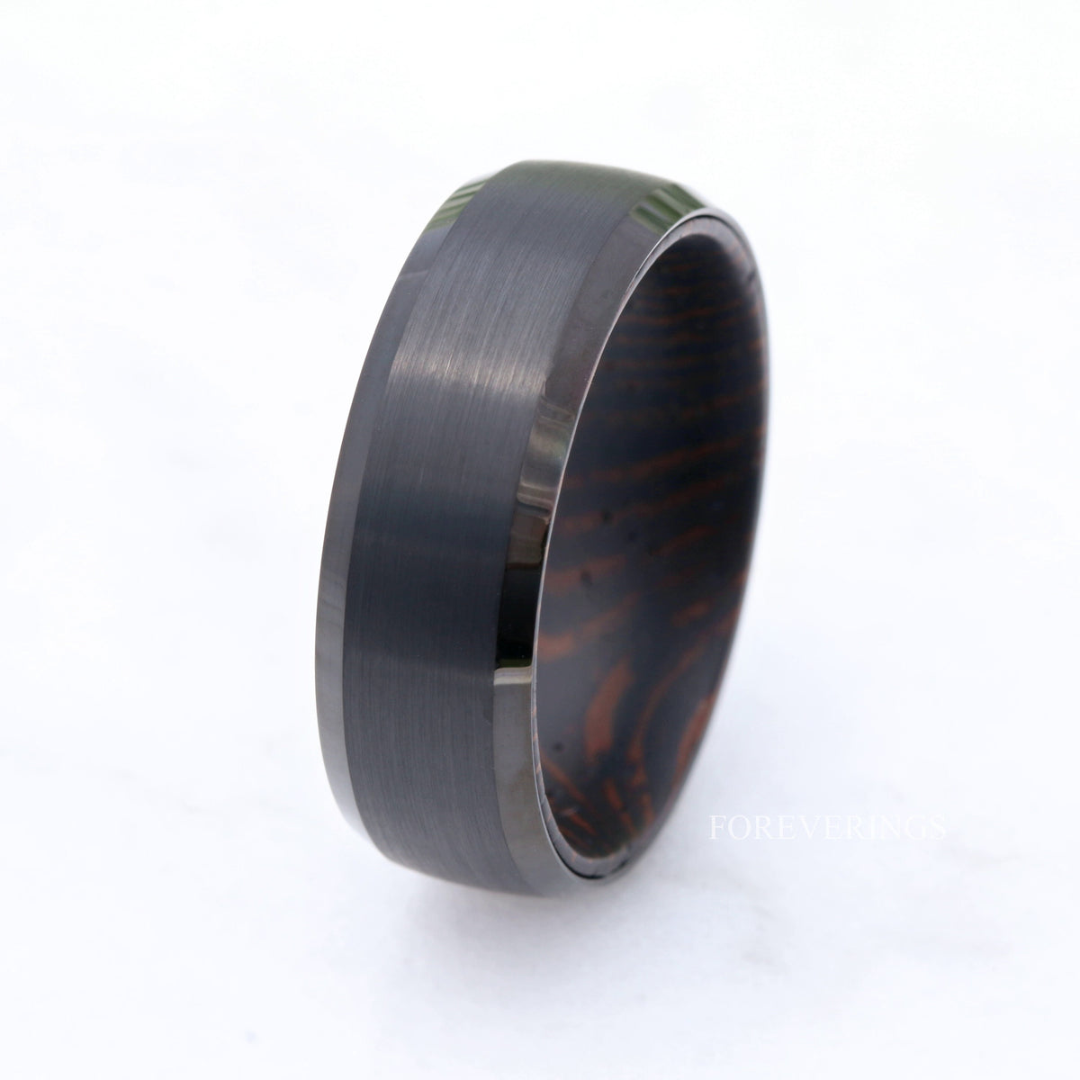 Black tungsten wenge wood band standing on a white surface, seen from farther back
