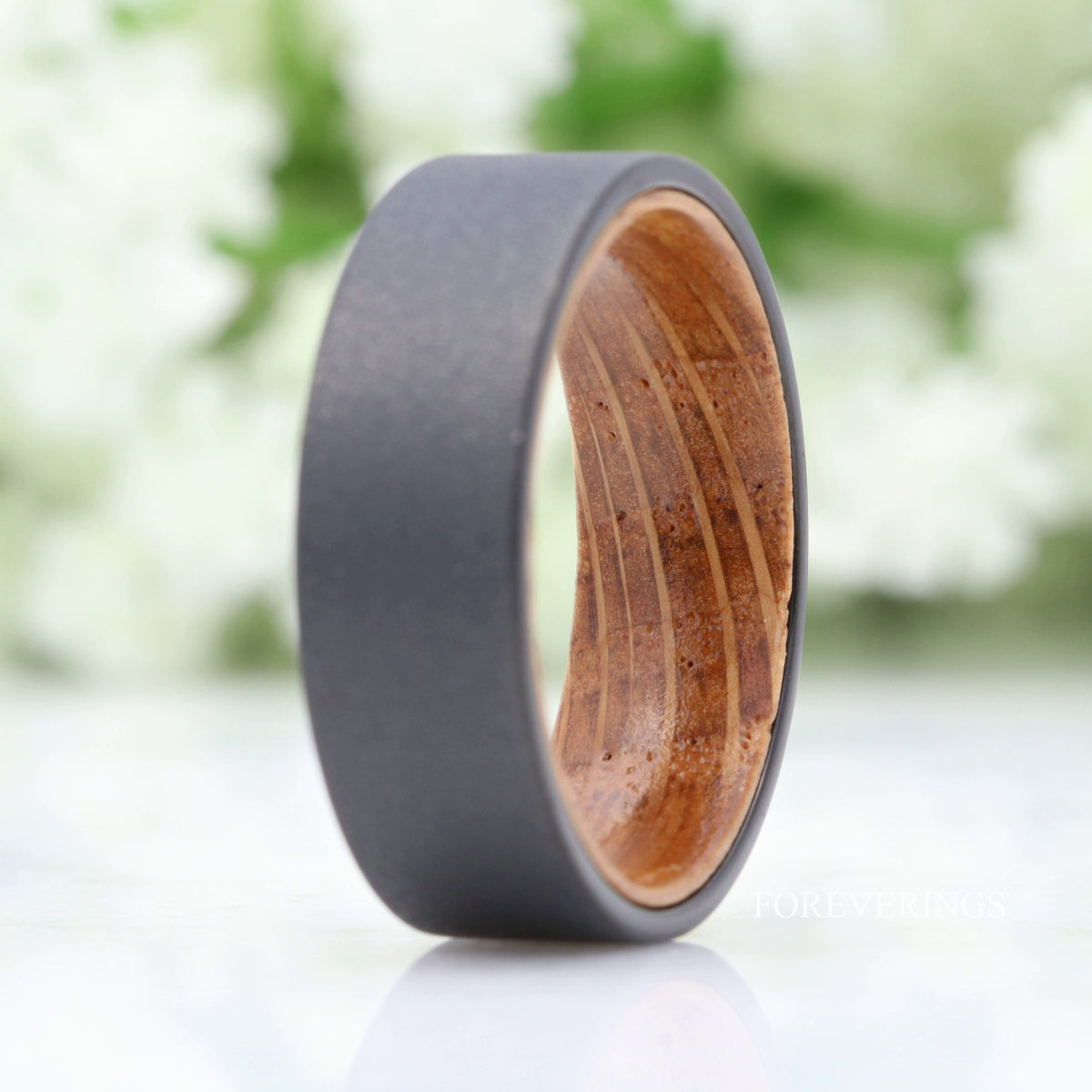 Sandblasted black tungsten whiskey barrel band standing upright, straight on with a reflection