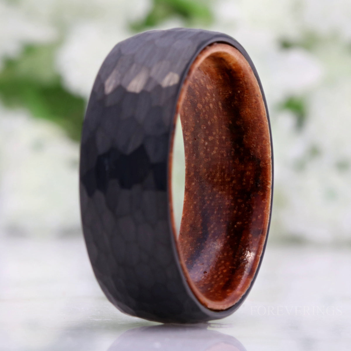 Hammered black tungsten zebra wood band standing upright in a wider view