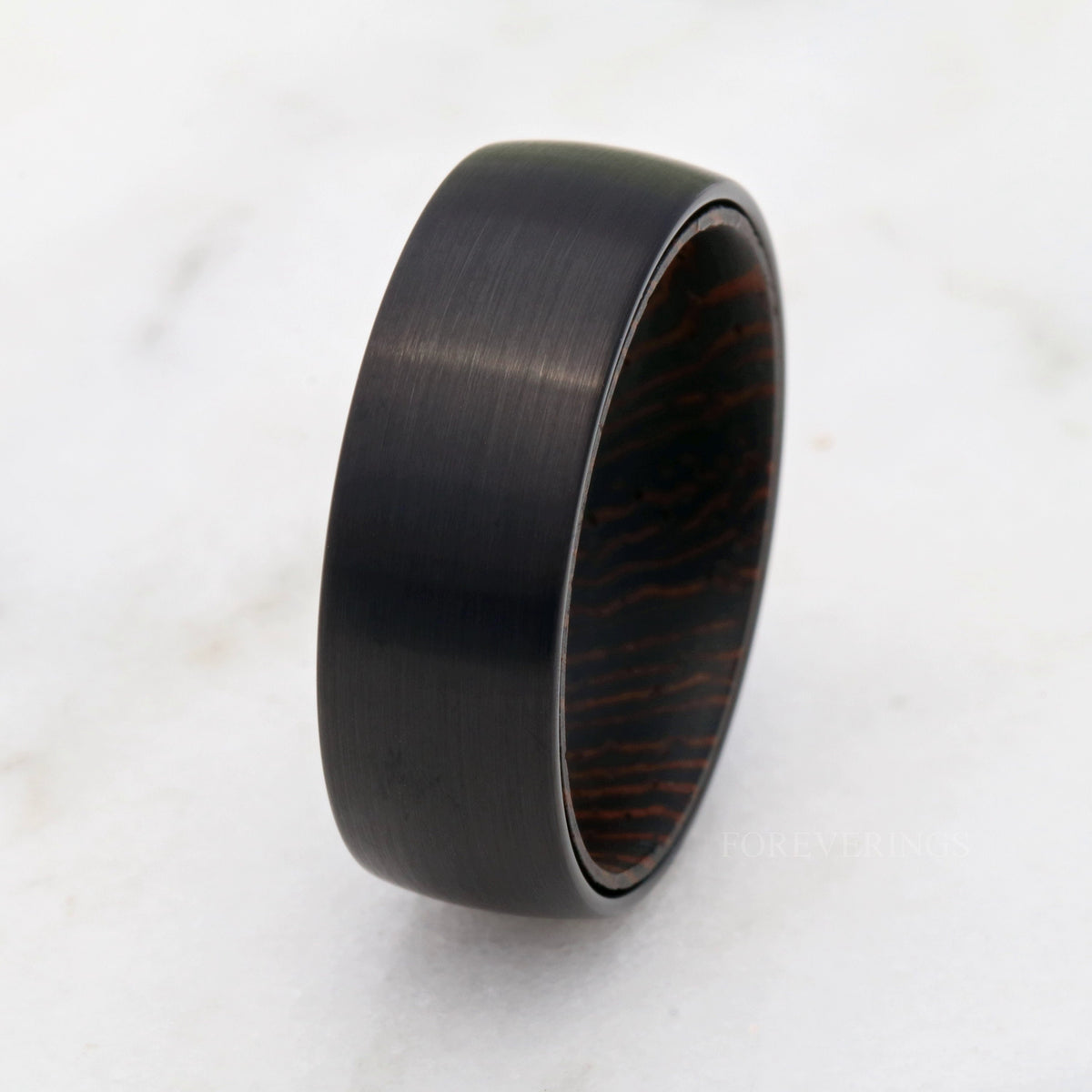8mm black tungsten wedding band angled from above, dark wenge wood grain inside