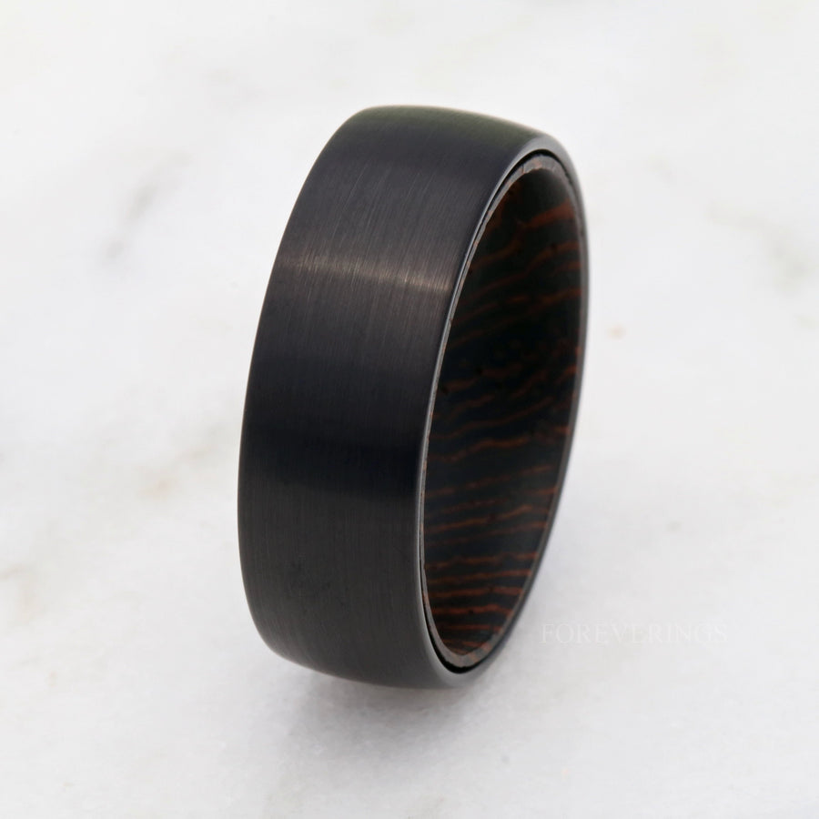 8mm black tungsten wedding band angled from above, dark wenge wood grain inside