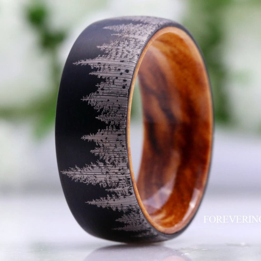Men's brushed black tungsten band with a pine tree pattern and olive wood interior, close-up