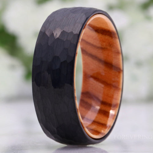 Men's 8mm hammered black tungsten band with olive wood interior, standing in a close crop