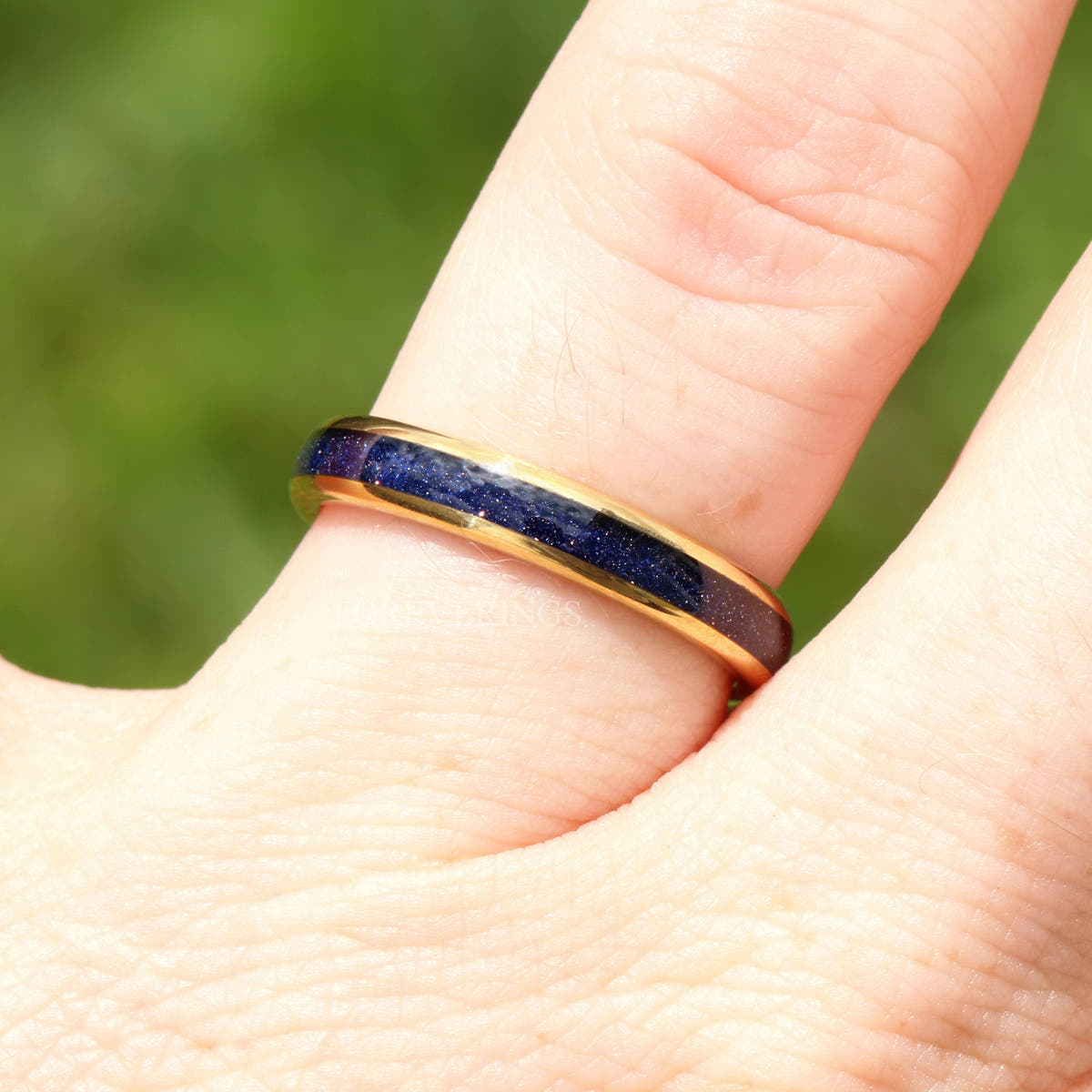 Gold tungsten blue sandstone ring worn on a finger, angled side view