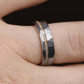 Hammered silver tungsten band with a white fire opal stripe worn on a finger, close view