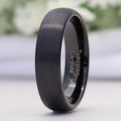 Men's 6mm matte black tungsten wedding band with a brushed dome, standing on edge in a close crop