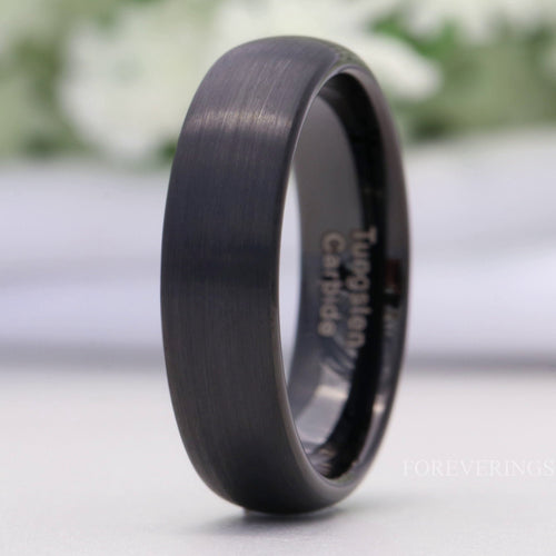 Men's 6mm matte black tungsten wedding band with a brushed dome, standing on edge in a close crop