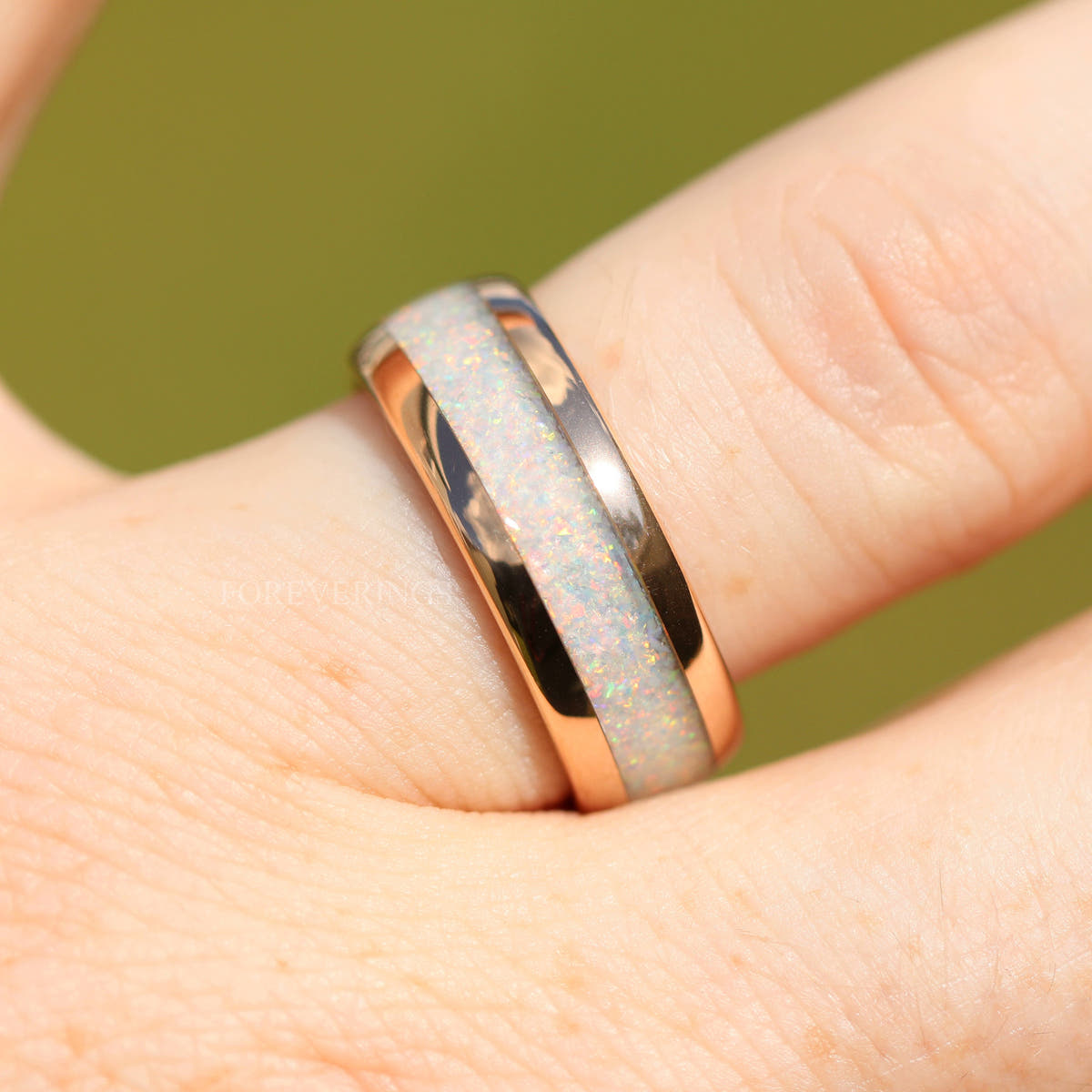Rose gold tungsten ring with white fire opal inlay worn on a finger, close-up