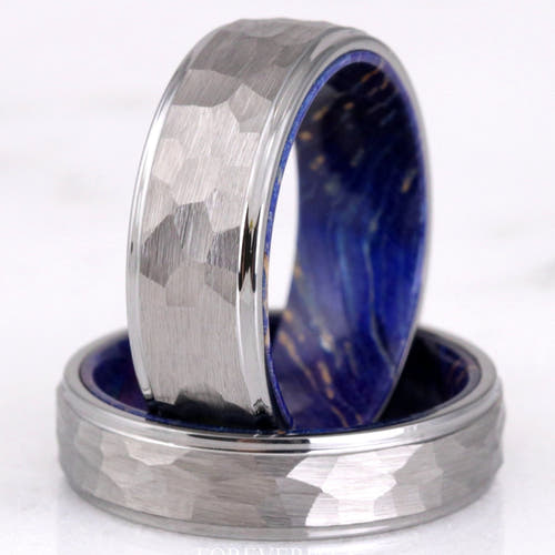 Men's hammered silver tungsten wedding bands lined with blue elder wood, one standing on the other
