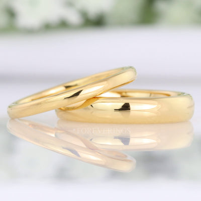 Minimalist 2mm and 4mm gold tungsten wedding bands with a polished dome, the thin band leaning on the wide one