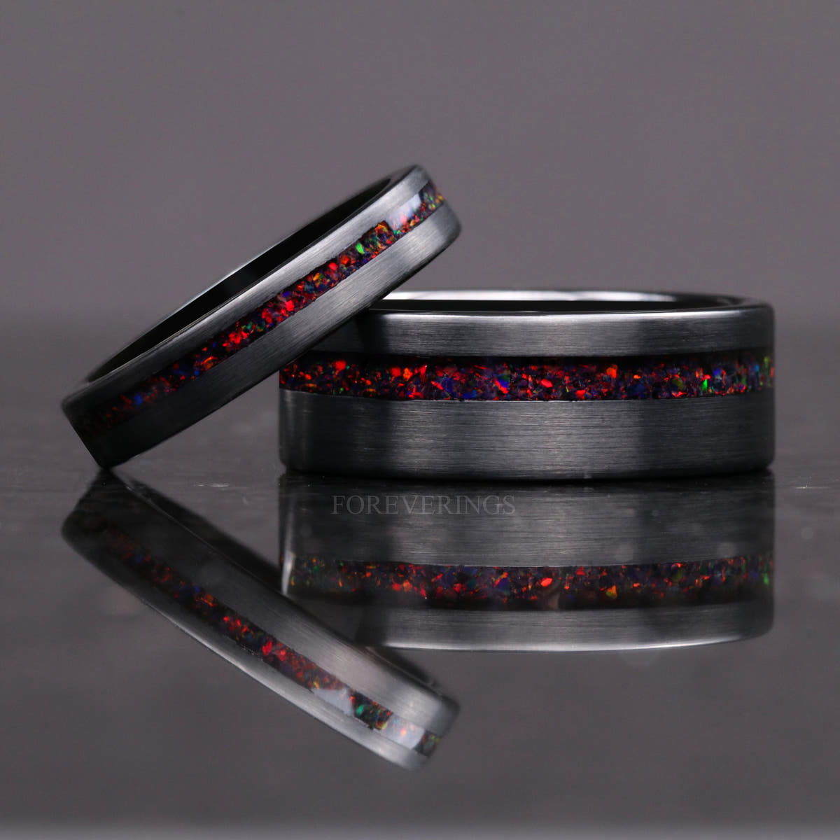 8mm brushed black tungsten fire opal ring with a thinner opal ring leaning on it