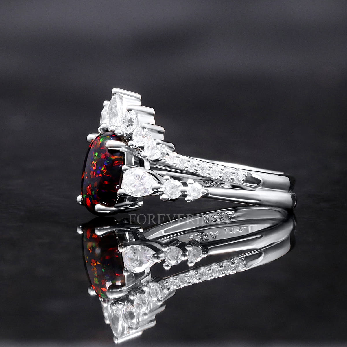 Black fire opal engagement ring from the side, showing the curved band of pear-shaped clear stones