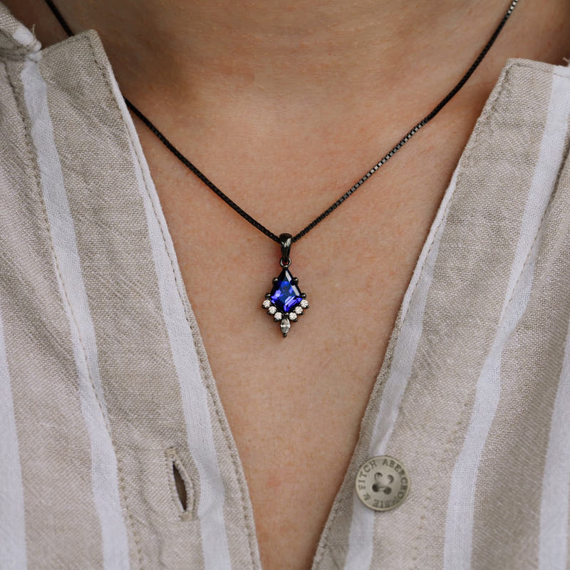 Kite cut blue sapphire pendant necklace worn at the neckline, close crop