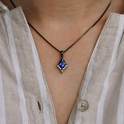 Kite cut blue sapphire pendant necklace worn at the neckline, close crop