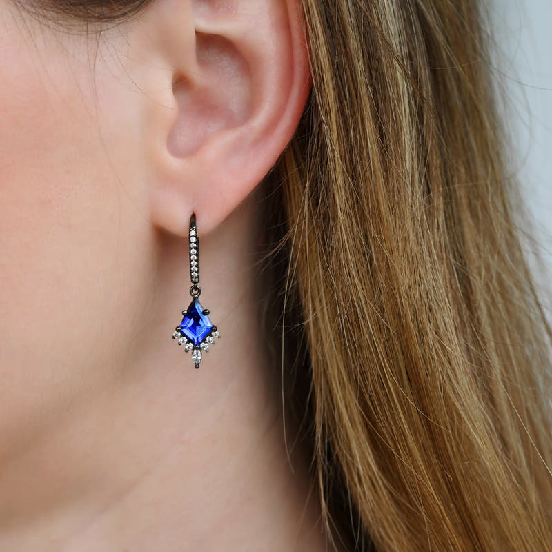 Black sterling silver blue sapphire drop earring worn on the ear, close-up
