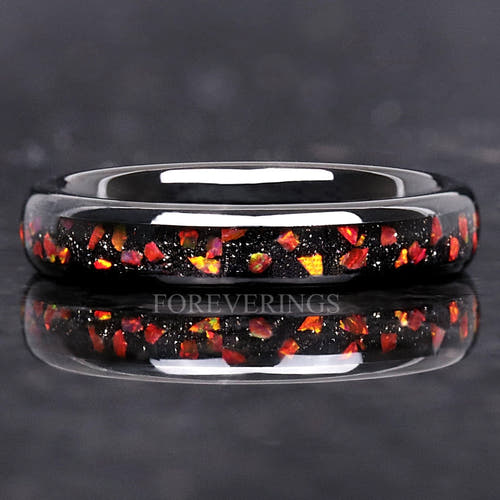 4mm black tungsten wedding ring with crushed red fire opal inlay, lying flat with a reflection