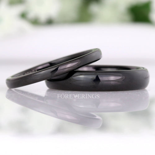 Polished black tungsten wedding bands in 2mm and 4mm, the thin band leaning on the wider one