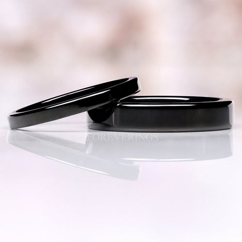 Flat black tungsten wedding bands in 2mm and 4mm, one resting on the other