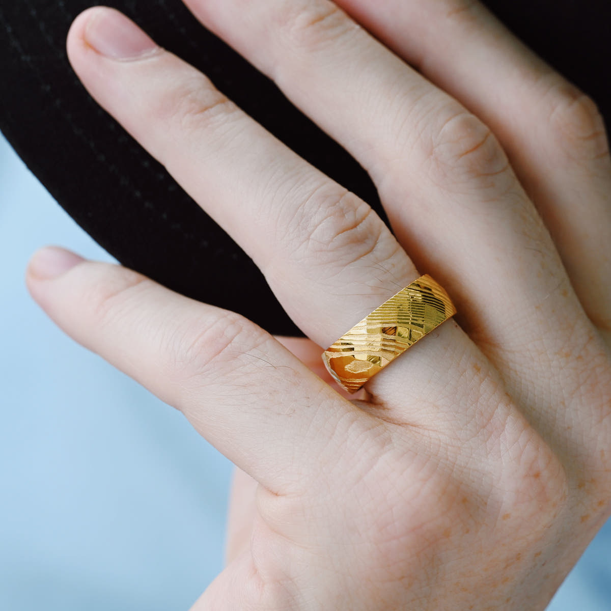 Gold Damascus steel wedding band worn on a hand, faceted surface catching the light