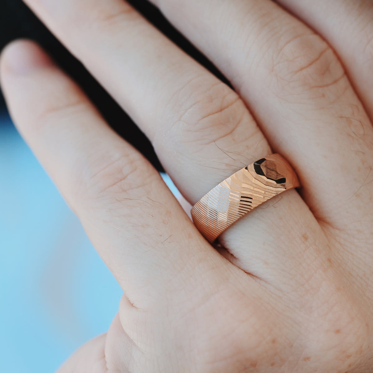 Hammered rose gold Damascus steel band worn on a finger, close crop