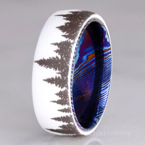 Men's 8mm white ceramic band with a forest tree-line design and blue Timascus inner sleeve, standing upright