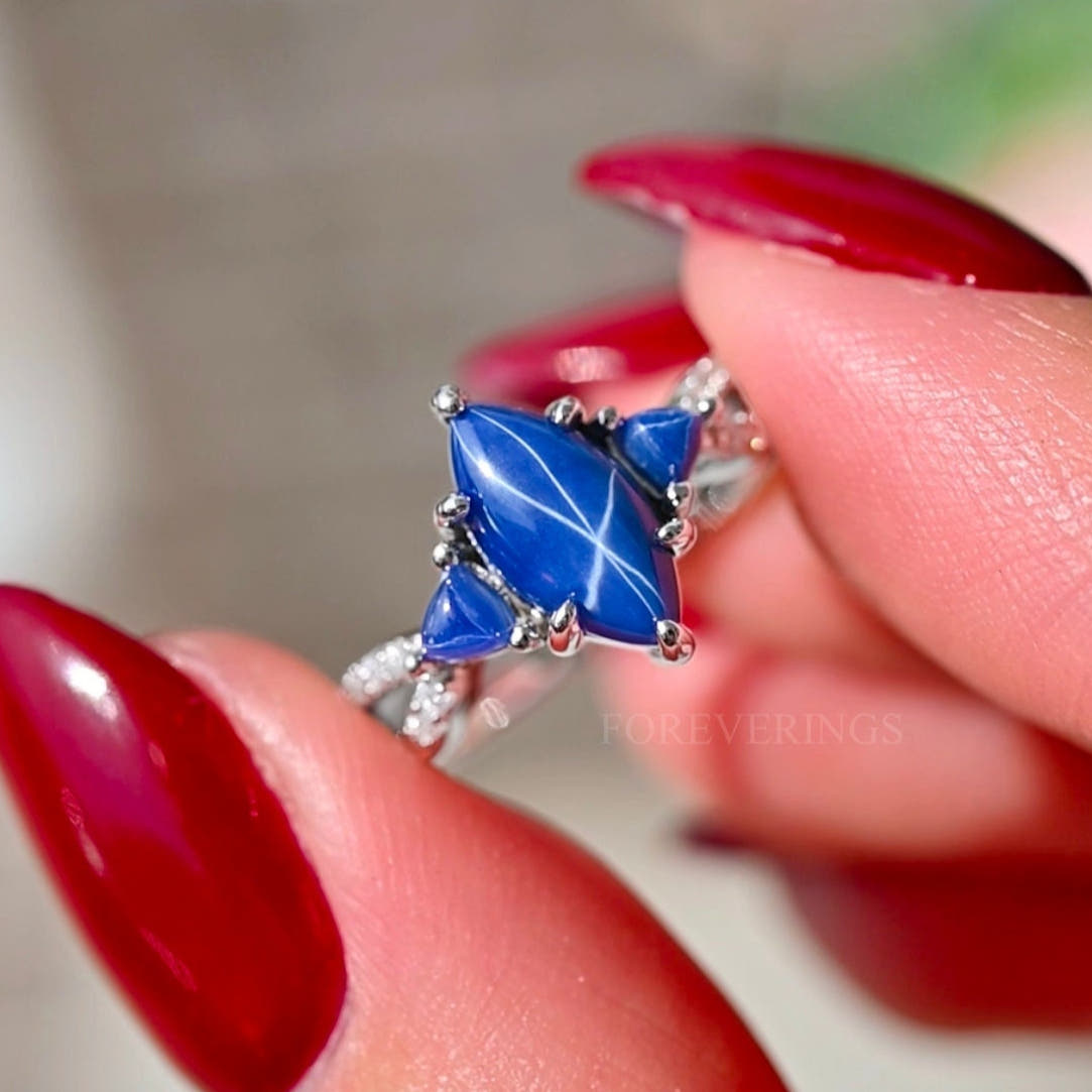 Women's sterling silver blue star sapphire ring held in fingertips, six-ray star visible