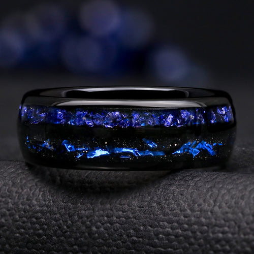 Black tungsten ring shown straight on, crushed blue sapphire above black sandstone with blue foil