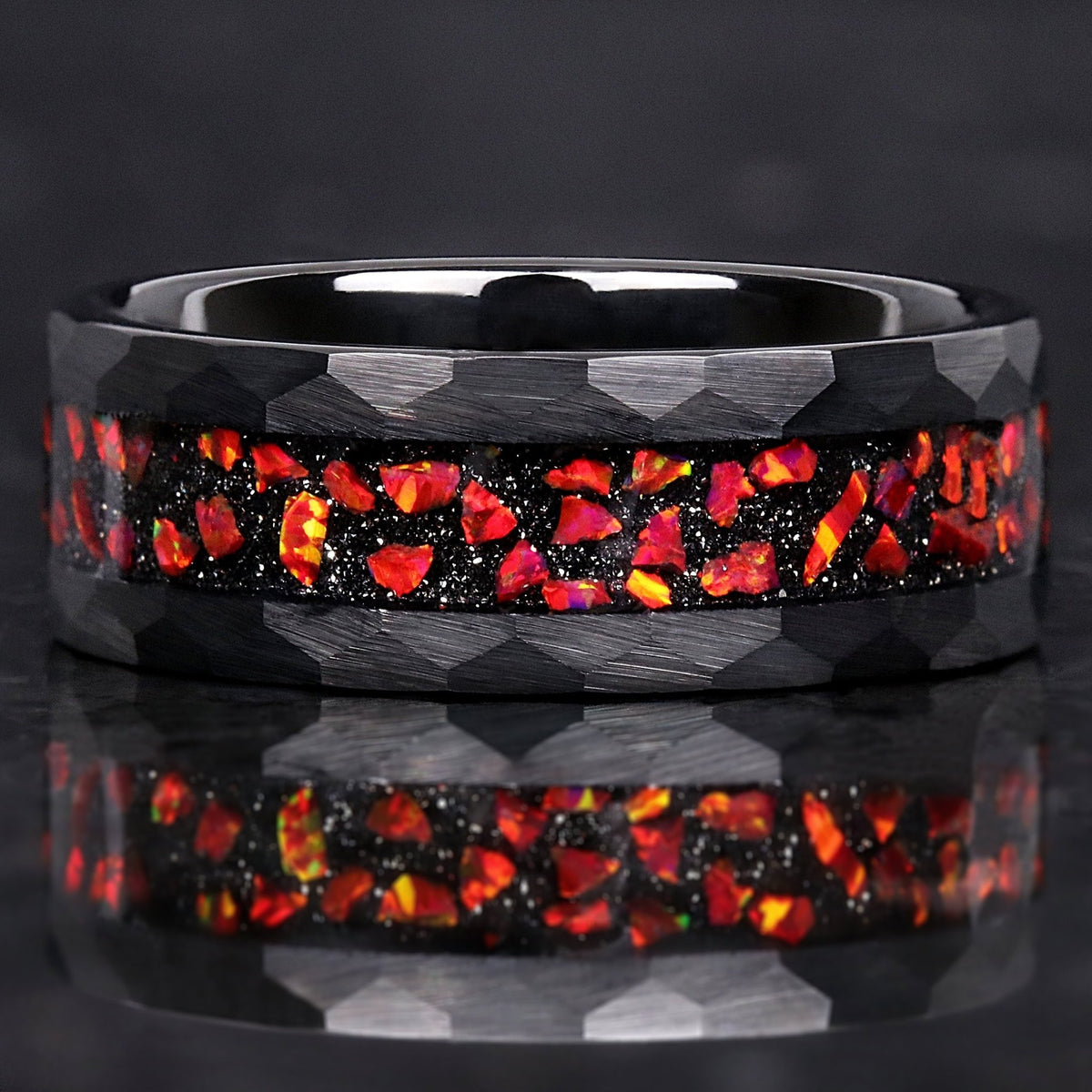 Men's 8mm hammered black tungsten ring with crushed red fire opal inlay, lying flat with a reflection