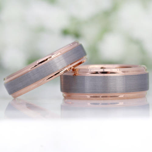 Two men's two-tone silver and rose gold tungsten wedding bands, one leaning on the other