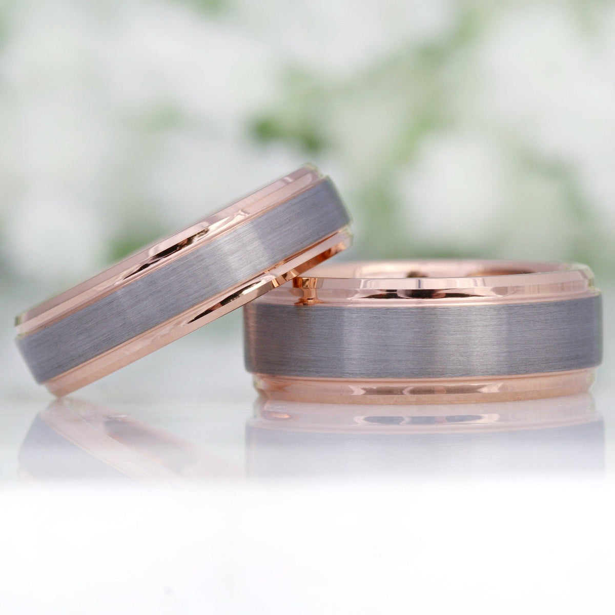Two men's two-tone silver and rose gold tungsten wedding bands, one leaning on the other