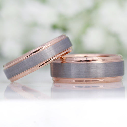 Two men's two-tone silver and rose gold tungsten wedding bands, one leaning on the other