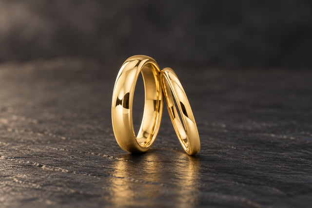 Two plain polished gold tungsten wedding bands, 4mm and 2mm, on dark slate