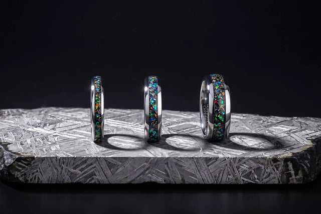 Three tungsten bands with meteorite and opal inlay standing on an etched meteorite slab