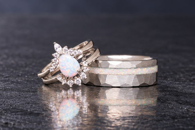 White fire opal couples ring set on dark slate: her pear opal ring beside his hammered silver band with opal inlay