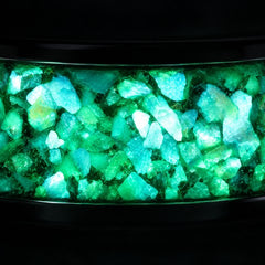 Close-up of a green glow-in-the-dark inlay lit up in a black tungsten band