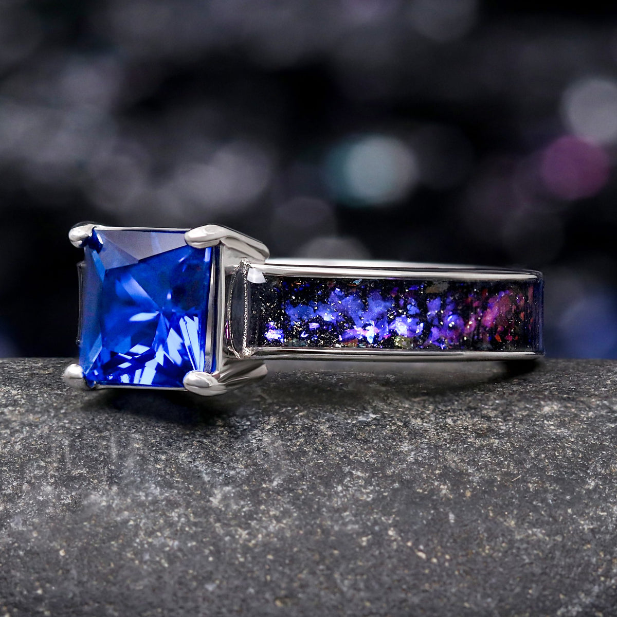Princess cut blue sapphire ring in sterling silver with Orion nebula inlay, angled to show the prongs