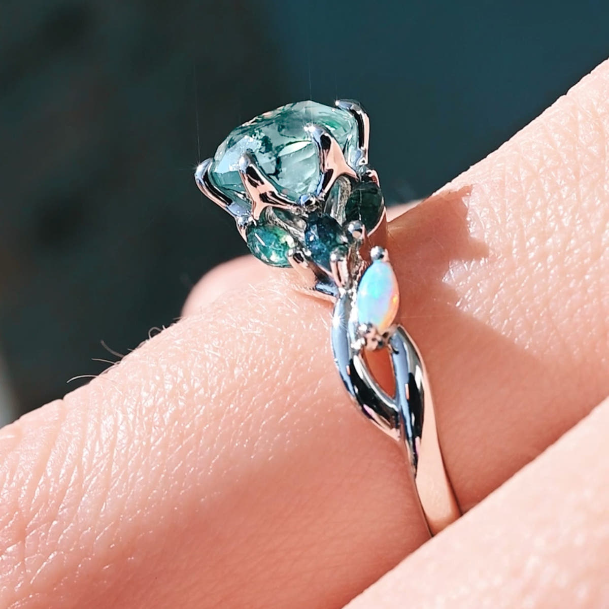 Sterling silver moss agate ring with a leaf vine band worn on a finger, angled view